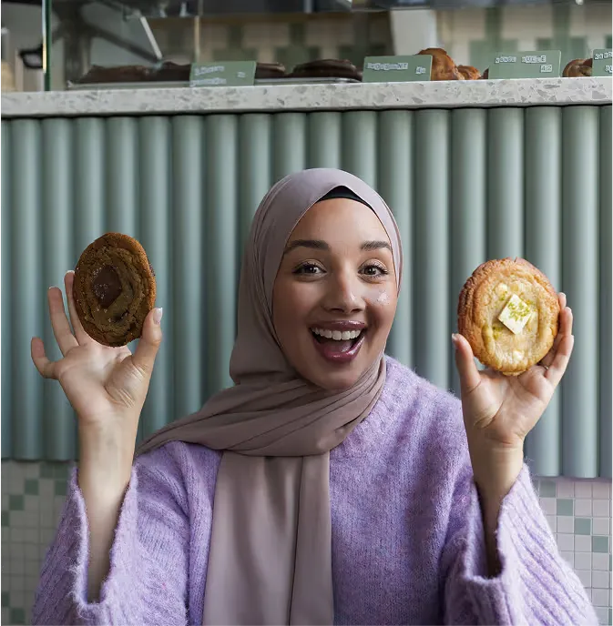 Camilla Hamid skrattar och håller upp två cookies i kaféet